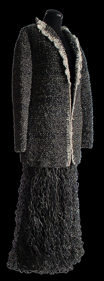 . Suit composed by a black cardigan  with a white-edged  collar. The jacket is knitted with black ads, the collar is crocheted with the white edge of dailies  with daisy motif. The transparent skirt (2011) is made with the black parts  of newspapers.